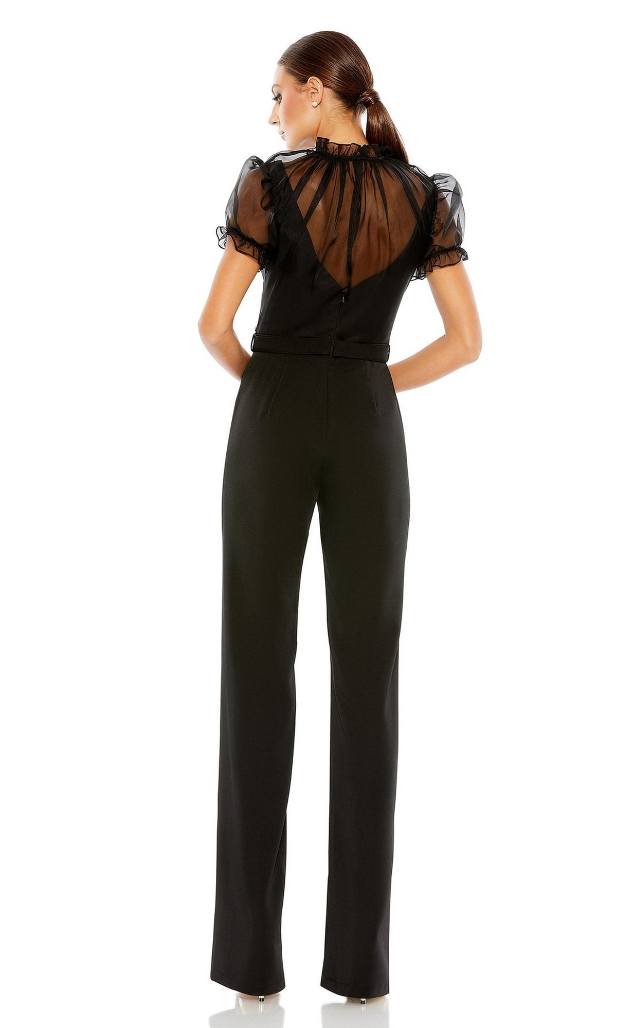 Woman with hair in a low ponytail stands with back to camera, wearing the Long Formal Jumpsuit 26621 by Mac Duggal. This style features a high neck, sheer puff sleeves, sheer upper back panel, and an elegant belted waist.
